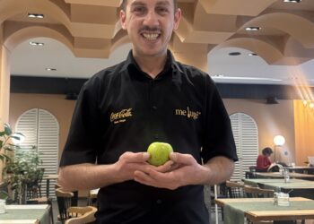 Jeton Musa holding a green apple at Meluge, with Chancellor Speedy praising his service as part of The Owner Schools' grassroots approach to supporting small businesses.